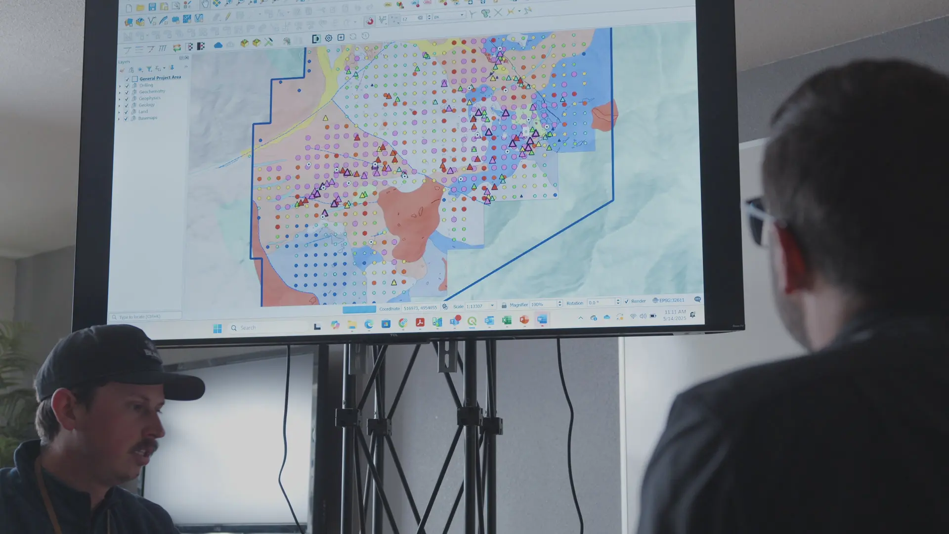 Two people in front of a screen with a map of drilling sites and data points