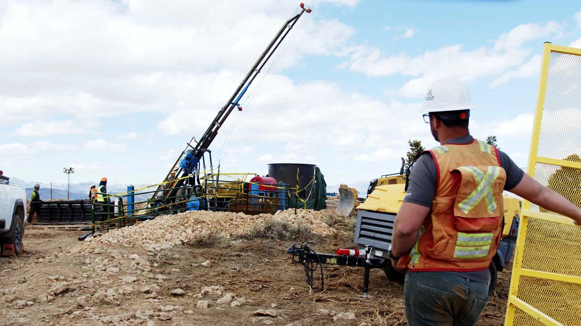 A worker in a Scout hardhat and a safety vest overlooks a drilling operation
