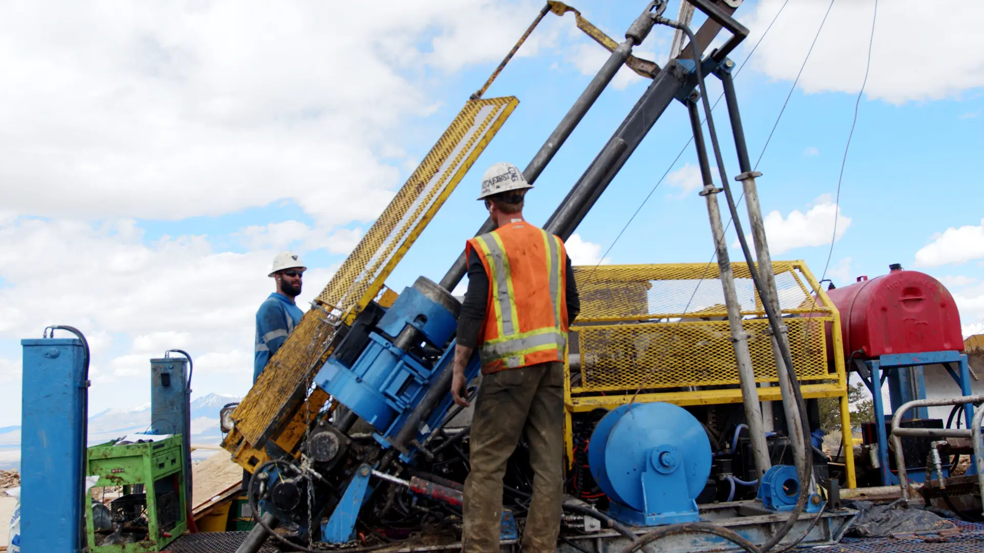 Workers in hard hats and safety vests standing near a drill